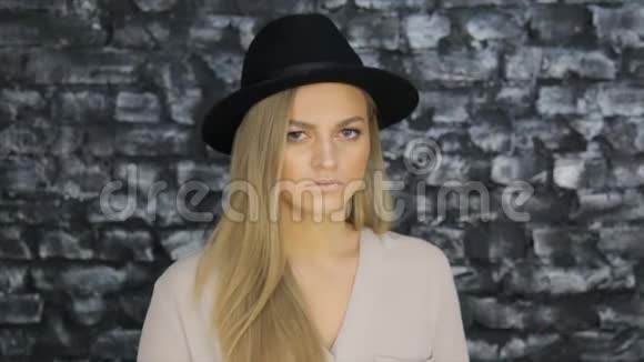 一个戴着黑帽子穿着灰色衬衫的女孩在砖墙背景下摆姿势视频的预览图