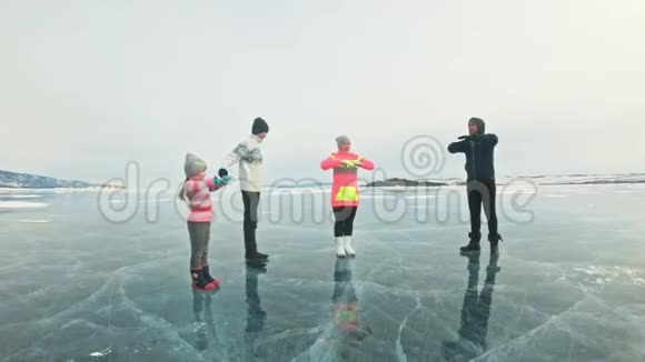 家庭在大自然中冰上做运动父亲在冬天训练他的家人母女和儿子看着他视频的预览图