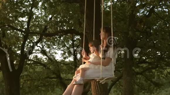 妈妈在阳光下摇动她的女儿特写镜头妈妈和宝宝骑在橡树树枝上的绳子上视频的预览图