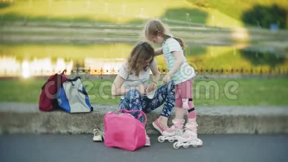 妈妈帮女儿戴上头盔和防护用具在公园里溜冰女人帮助女孩视频的预览图
