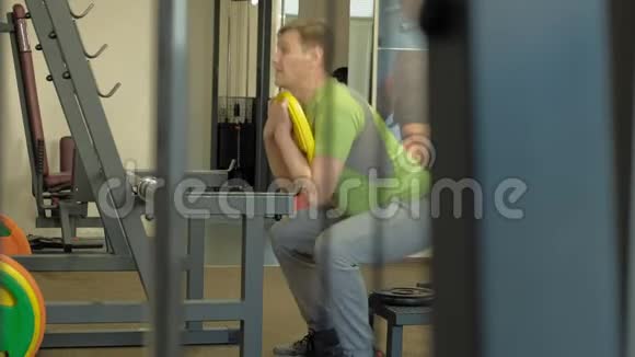 这个超重的人是用一个重量盘作为杠铃的蹲健身训练健康生活方式视频的预览图