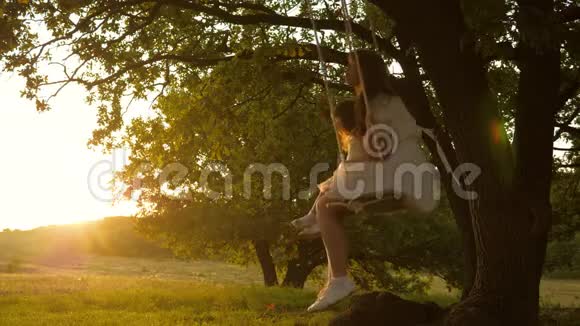 妈妈在阳光下摇动她的女儿母亲和婴儿在森林中的橡树枝上骑着一条绳秋千视频的预览图