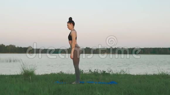 年轻女孩穿着运动服早上在湖里和科普空间做瑜伽视频的预览图