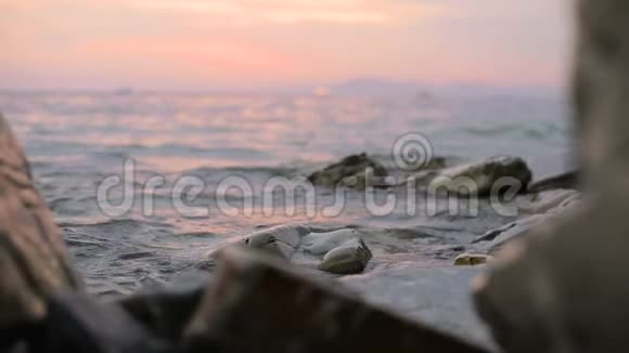 特写慢动作低角度小海浪在岩石海滩上翻滚海边傍晚在卵石岩石海滩上日落视频的预览图