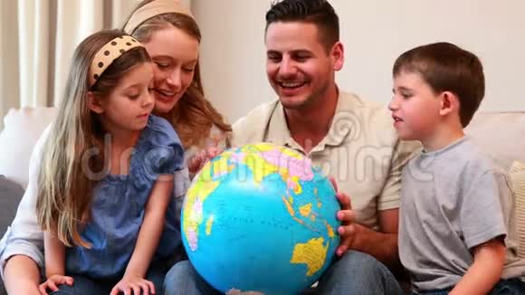 幸福的年轻家庭坐在沙发上看地球仪视频的预览图