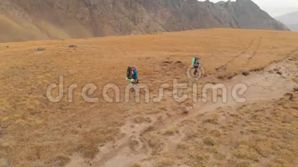 一对戴着帽子和太阳镜的大背包的旅行者男女在高山上漫步的鸟瞰图视频的预览图