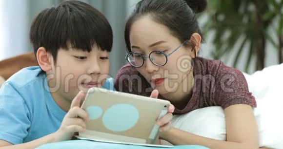 年轻的亚洲母亲带着儿子一起在家看平板电脑玩平板电脑视频的预览图