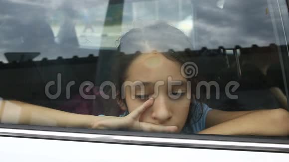 小女孩无聊地坐在车里透过窗户向窗外看街道的倒影视频的预览图