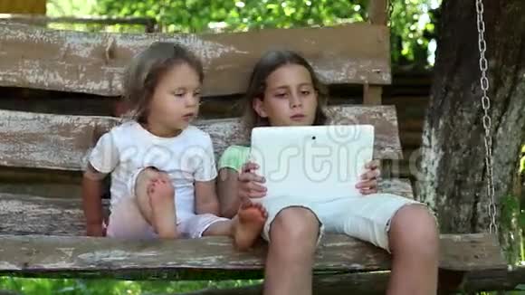 两个拿着平板电脑的女孩坐在秋千凳上视频的预览图