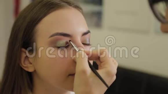 专业的眼妆发型师化妆师将化妆应用于一个年轻的女人在美容院有一个特殊的刷子视频的预览图