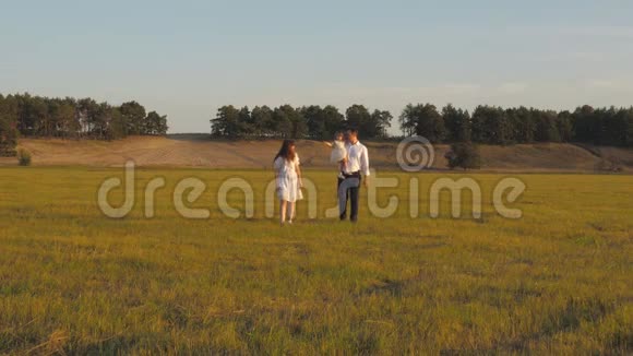 妈妈爸爸和小女儿在阳光下的田野里散步快乐童年的概念孩子爸爸妈妈玩视频的预览图