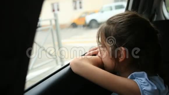小女孩无聊地坐在车里透过窗户向窗外看街道的倒影视频的预览图