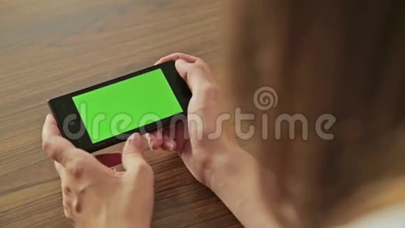 漂亮的女人手里拿着绿色屏幕显示的智能手机视频的预览图