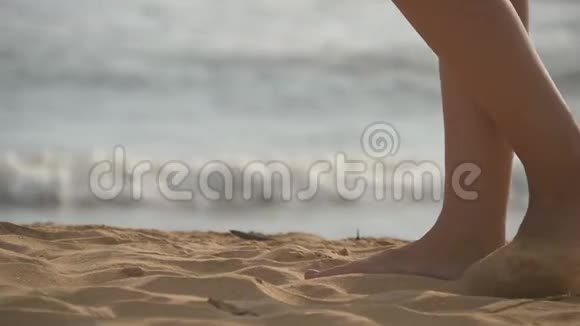 靠近女性的脚在沙滩上金色的沙滩上行走背景是海浪年轻女子的腿视频的预览图