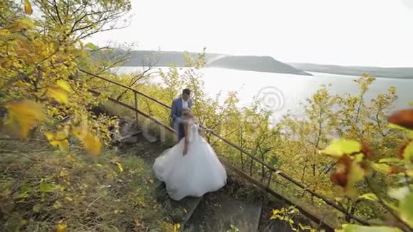 年轻漂亮的新婚夫妇一起在河边的公园里可爱的新郎和新娘结婚纪念日慢动作视频的预览图