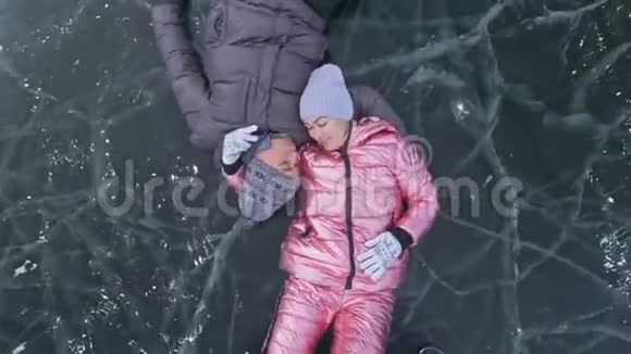 在冰封的湖面上年轻夫妇在冬天散步时玩得很开心恋人们躺在冰面上有裂缝视频的预览图