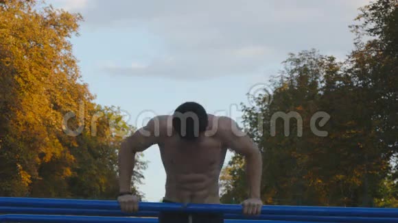 在城市公园的运动场运动员在双杠上做俯卧撑强壮的年轻肌肉男在户外训练视频的预览图