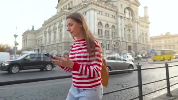 日落时分年轻女子用智能手机走在一条老街上通信社交网络网上购物视频的预览图