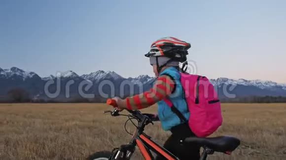 一个高加索儿童骑着自行车在麦田里行走女孩在美丽的白雪公主的背景下走着黑色橙色的自行车视频的预览图