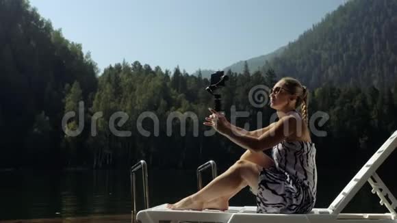 女性拍摄手持电影万向节稳定智能手机女孩躺在码头晒太阳自拍博客视频的预览图
