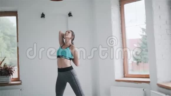穿着运动服的年轻黑发女孩在家里的明亮房间里做运动视频的预览图