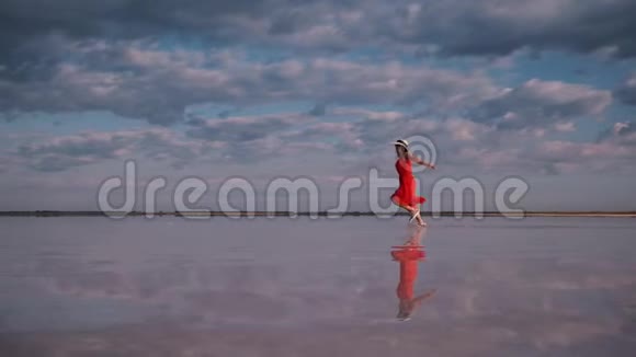 穿着飘舞裙的女孩沿着一个盐湖奔跑云彩反射在水中视频的预览图
