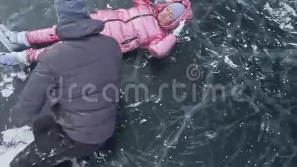 在冰封的湖面上年轻夫妇在冬天散步时玩得很开心恋人们躺在冰面上有裂缝视频的预览图