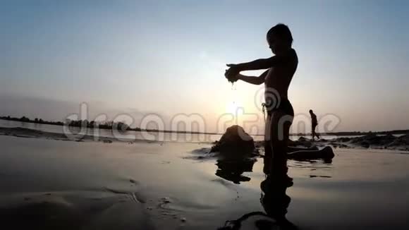 海滩儿童剪影在日落时建造沙堡视频的预览图