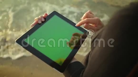 女人在海边的绿色屏幕上使用平板电脑视频的预览图