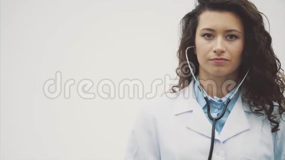 幸福的年轻微笑女孩医生的肖像穿着白色长袍站在灰色的背景上在此期间视频的预览图
