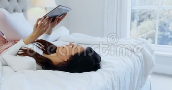 女性在床上放松时使用数码平板电脑视频的预览图
