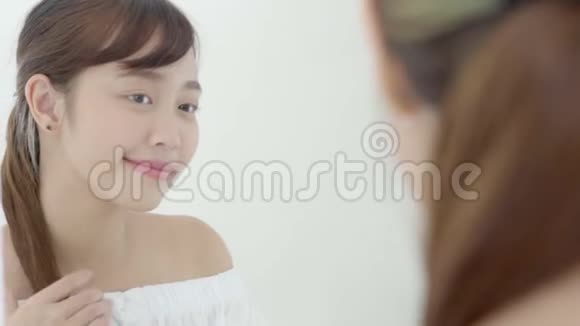美丽的肖像年轻的亚洲女人微笑着看着镜子检查皮肤护理白种人在卧室健康视频的预览图