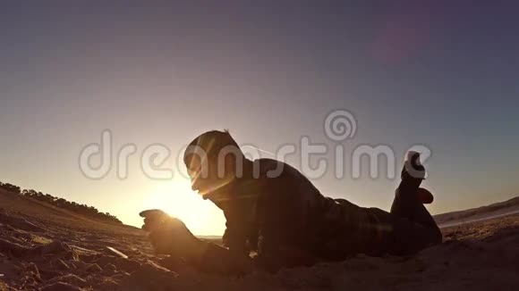 便携式控制台男人躺在沙滩上在日落阳光下的便携式游戏机里玩耍视频的预览图