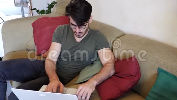 年轻人在沙发上做笔记本电脑作业视频的预览图