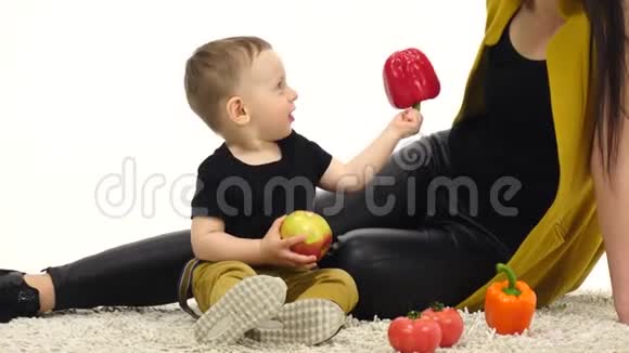 妈妈和儿子坐在地上拿着蔬菜白色背景视频的预览图