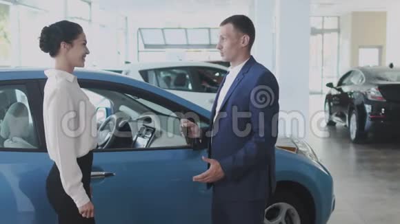 售货员把车钥匙给了汽车经销店里快乐的女商人视频的预览图