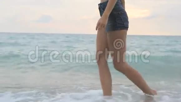 夕阳西下年轻漂亮的晒黑女孩金发穿着牛仔短裤沿着海滨散步视频的预览图