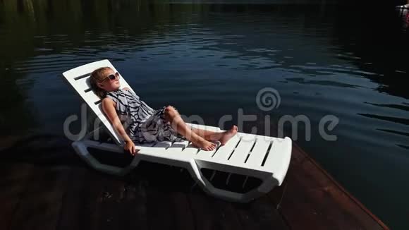 小女孩躺在日光浴床上戴着太阳镜和一条薄纱披肩儿童在洪水木水下码头休息人行道视频的预览图