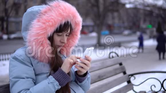 冬天一个穿着灰色保暖夹克的年轻女人在街上用电话视频的预览图