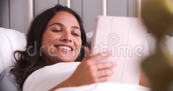 使用数码平板电脑躺在床上的年轻女子视频的预览图