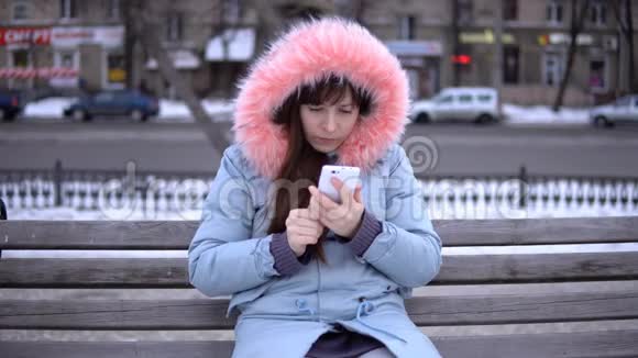 冬天一个穿着灰色保暖夹克的年轻女人在街上用电话视频的预览图