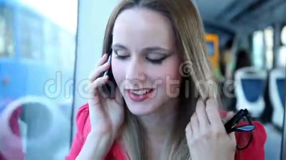 年轻的金发女子骑着电车在手机手机手机上说话拿着眼镜视频的预览图
