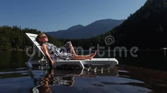 小女孩躺在日光浴床上戴着太阳镜和一条薄纱披肩儿童在洪水木水下码头休息人行道视频的预览图