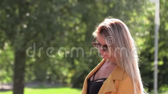 穿着黄色夹克黑色连衣裙和太阳镜的漂亮金发女郎视频的预览图