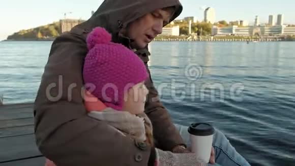 男人和女孩父亲和女儿坐在河港喝茶野餐笑穿着暖和的衣服视频的预览图