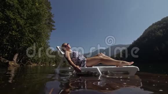 女人躺在太阳床上戴着太阳镜和一条薄纱披肩女孩在洪水木水下码头休息路面是视频的预览图