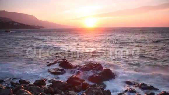 日出时波浪围绕着石头破碎视频的预览图