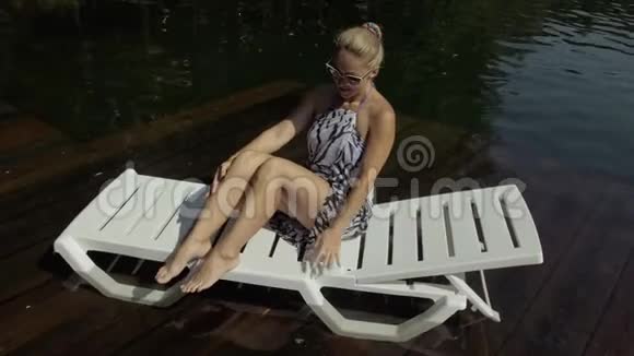 女人躺在日光浴床上戴着太阳镜和一条薄纱披肩女孩在洪水木水下码头休息路面是视频的预览图