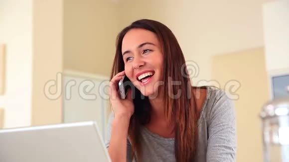 漂亮的黑发女人坐着用笔记本电脑和电话视频的预览图