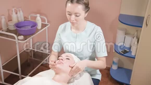 戴着面具和手套的女美容师给一个有魅力的女人做一个有益健康的面部按摩新一代视频的预览图